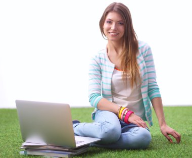 Laptoplu genç bir kadın yeşil çimlerde oturuyor.