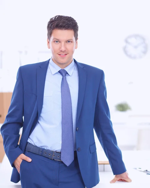Hombre de negocios o gerente de pie contra su escritorio en la oficina con los brazos cruzados —  Fotos de Stock