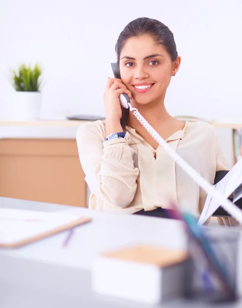 Jonge zakenvrouw zit aan het bureau en praat over de telefoon — Stockfoto