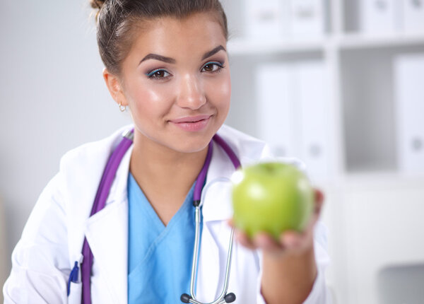 Женщина-врач держит за руку зеленое яблоко, сидит