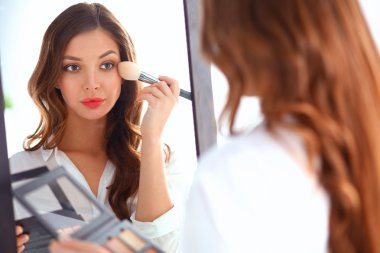 Genç ve güzel bir kadın aynanın yanında makyaj yapıyor.