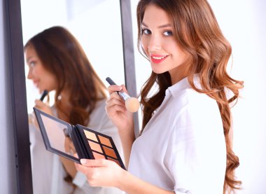 Genç ve güzel bir kadın aynanın yanında makyaj yapıyor.