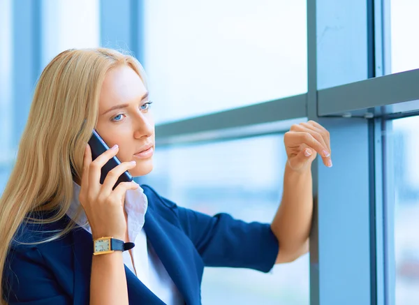 Podnikatelka stojí proti oknu kanceláře a mluví na mobilním telefonu — Stock fotografie