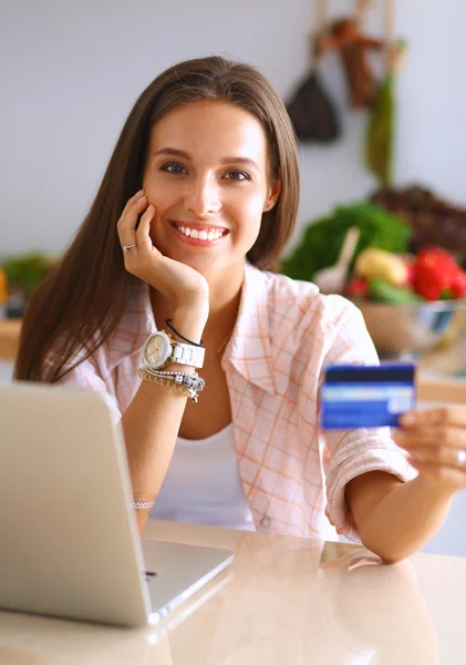 Mulher sorrindo compras on-line usando tablet e cartão de crédito na cozinha — Fotografia de Stock