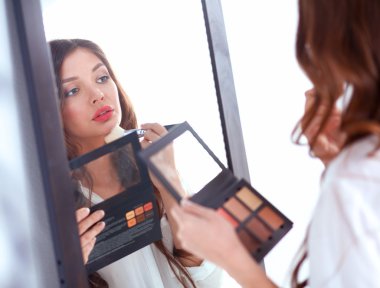 Genç ve güzel bir kadın aynanın yanında makyaj yapıyor.