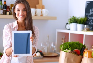 Mutfakta yemek yapmak için tablet bilgisayar kullanan genç bir kadın.