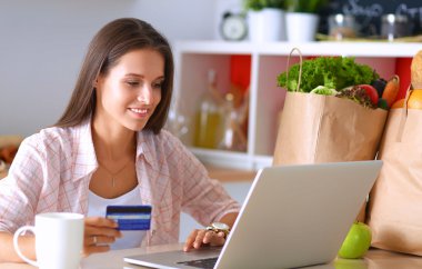 Gülümseyen kadın mutfakta tablet ve kredi kartı kullanarak alışveriş online