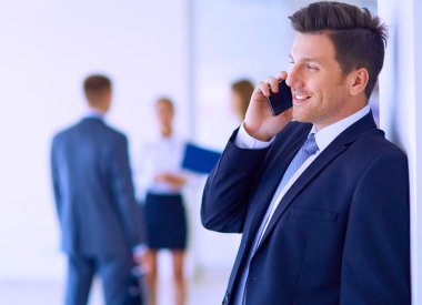 Ofisteki genç iş adamının portresi. Arka planda meslektaşları var ve cep telefonu kullanıyor.