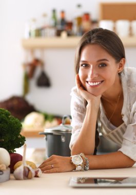Mutfakta yemek yapmak için tablet bilgisayar kullanan genç bir kadın.