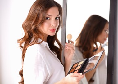 Genç ve güzel bir kadın aynanın yanında makyaj yapıyor.