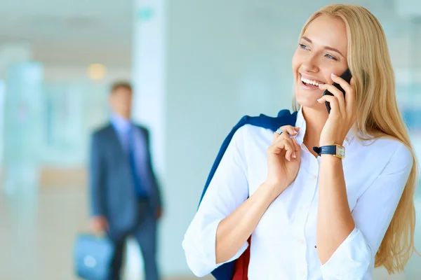 Affärskvinna står mot kontorsfönster talar på mobiltelefon — Stockfoto