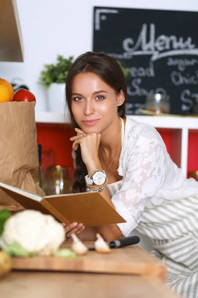 Jonge vrouw die kookboek leest in de keuken, op zoek naar recept — Stockfoto