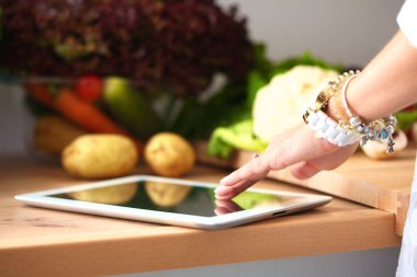 Mutfakta yemek yapmak için tablet bilgisayar kullanan genç bir kadın.