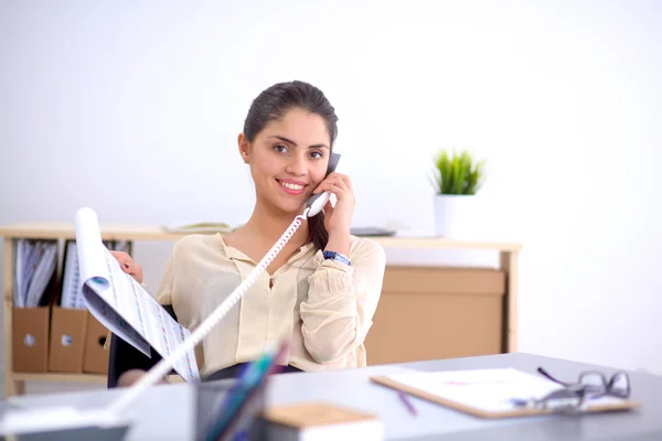 Jonge zakenvrouw zit aan het bureau en praat over de telefoon — Stockfoto