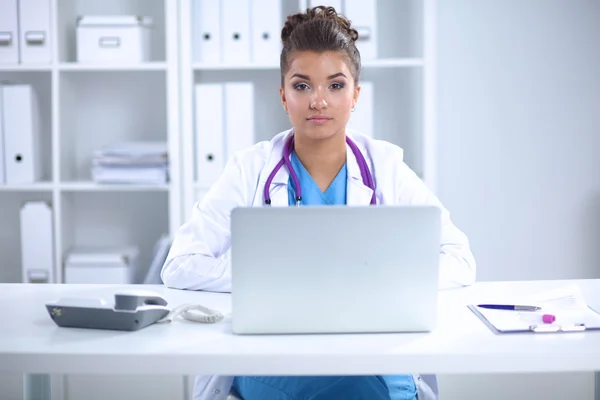 Όμορφη νεαρή χαμογελαστή γυναίκα γιατρός κάθεται στο γραφείο και γράφει. — Φωτογραφία Αρχείου