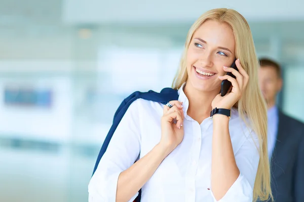 Zakenvrouw staat tegen kantoorraam te praten op mobiele telefoon — Stockfoto