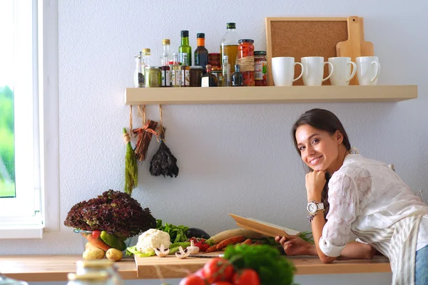 Ung kvinna läser kokbok i köket, letar efter recept — Stockfoto