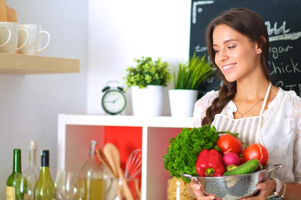 Souriante jeune femme tenant des légumes debout dans la cuisine — Photo