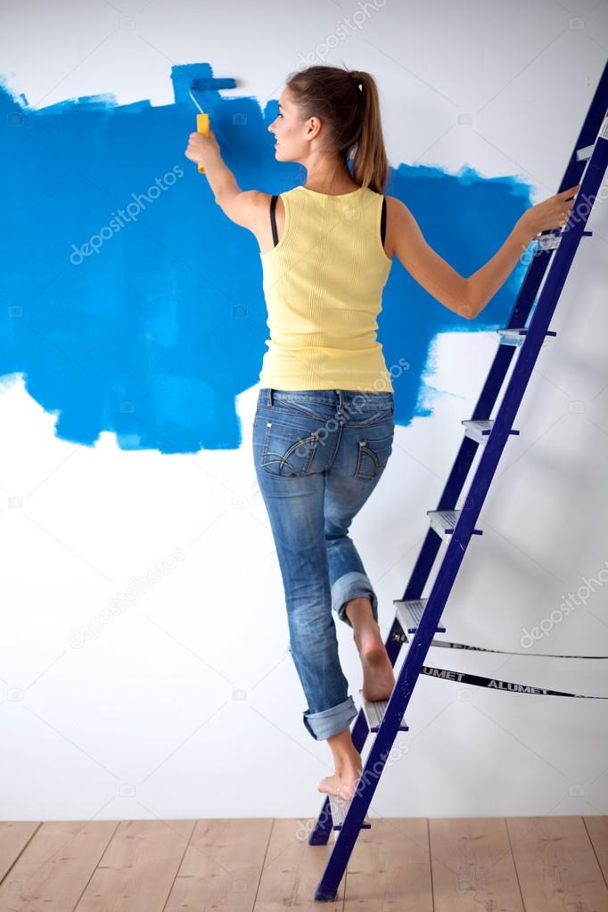 Beautiful young woman doing wall painting, standing near ladder
