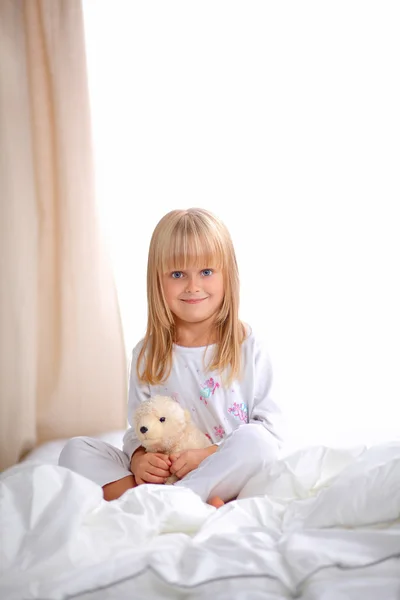 Menina com ursinho de pelúcia deitado na cama em casa — Fotografia de Stock