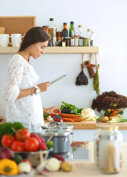 Young woman using a tablet computer to cook in her kitchen — Stock Photo, Image