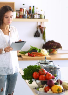 Mutfakta yemek yapmak için tablet bilgisayar kullanan genç bir kadın.
