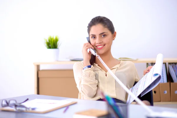 Joven mujer de negocios sentada en el escritorio y hablando por teléfono —  Fotos de Stock