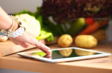 Mutfakta yemek yapmak için tablet bilgisayar kullanan genç bir kadın.