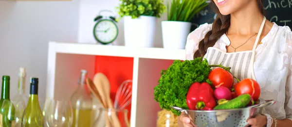 Mujer joven sonriente sosteniendo verduras de pie en la cocina —  Fotos de Stock