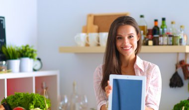 Mutfakta yemek yapmak için tablet bilgisayar kullanan genç bir kadın.