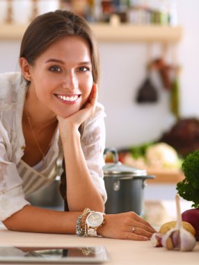 Mutfakta yemek yapmak için tablet bilgisayar kullanan genç bir kadın.
