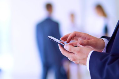 Ofisteki genç iş adamının portresi. Arka planda meslektaşları var ve cep telefonu kullanıyor.