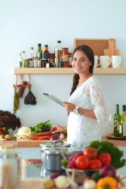 Mutfakta yemek yapmak için tablet bilgisayar kullanan genç bir kadın.