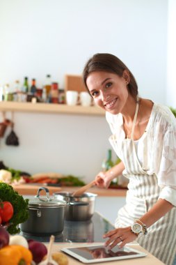 Mutfakta yemek yapmak için tablet bilgisayar kullanan genç bir kadın.