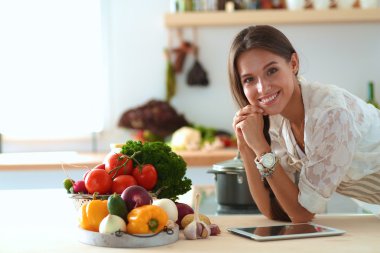 Mutfakta yemek yapmak için tablet bilgisayar kullanan genç bir kadın.