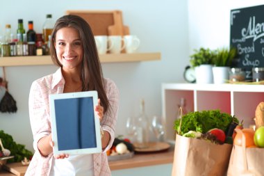 Mutfakta yemek yapmak için tablet bilgisayar kullanan genç bir kadın.