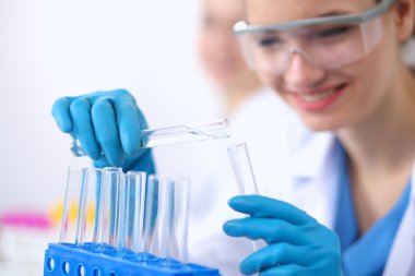 Kadın araştırmacı, beyaz arka planda izole edilmiş ilaç şişeleri ve mataralarla çevrili.