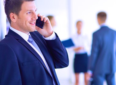 Ofisteki genç iş adamının portresi. Arka planda meslektaşları var ve cep telefonu kullanıyor.