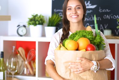 Elinde sebzeli alışveriş torbası tutan genç bir kadın.