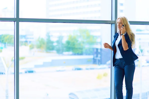 Mujer de negocios de pie contra la ventana de la oficina hablando por teléfono móvil —  Fotos de Stock