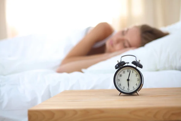 Joven mujer dormida y despertador en el dormitorio en casa —  Fotos de Stock