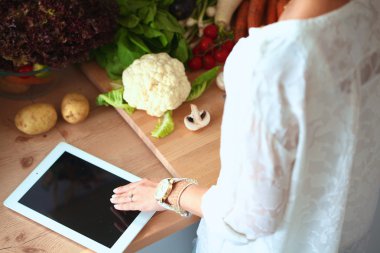 Mutfakta yemek yapmak için tablet bilgisayar kullanan genç bir kadın.