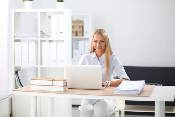 Attraktiv affärskvinna sitter på ett skrivbord med bärbar dator på kontoret — Stockfoto