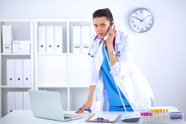 Mujer joven médico en bata blanca en el ordenador usando el teléfono —  Fotos de Stock