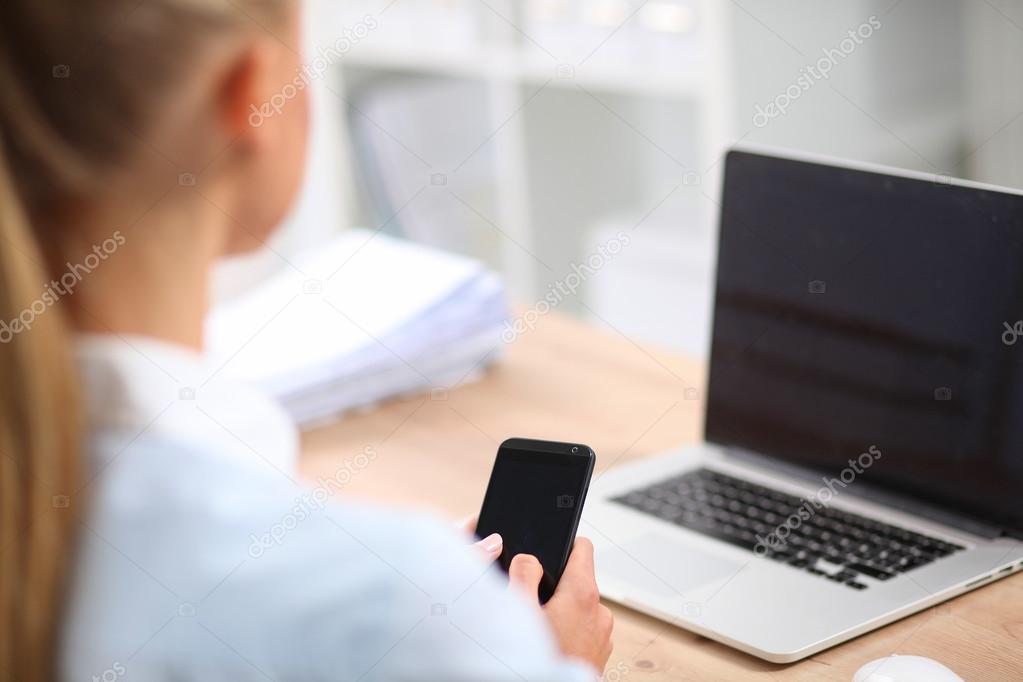 Businesswoman sending message with smartphone sitting in the office