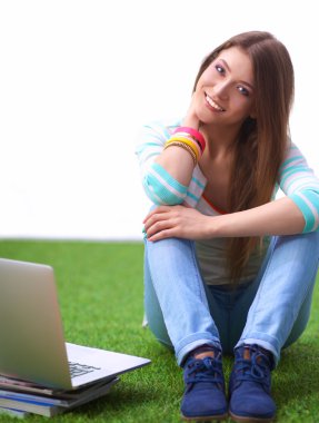 Laptoplu genç bir kadın yeşil çimlerde oturuyor.
