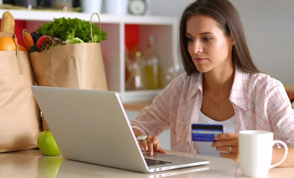 Mujer sonriente compras en línea utilizando la tableta y la tarjeta de crédito en la cocina —  Fotos de Stock