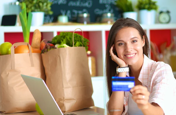 Mulher sorrindo compras on-line usando tablet e cartão de crédito na cozinha — Fotografia de Stock