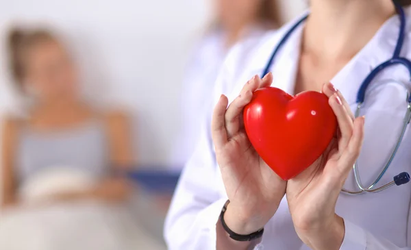 Mujer joven médico sosteniendo un corazón rojo, de pie sobre fondo gris — Foto de Stock