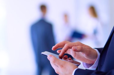 Ofisteki genç iş adamının portresi. Arka planda meslektaşları var ve cep telefonu kullanıyor.